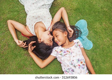 two indonesian sisters lying down on a grass - Powered by Shutterstock