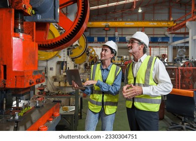 Two industrial workers engrossed in a discussion beside a high-tech assembly line machine, inside a bustling factory. Safety gear and intricate machinery enhance the sense of a reliable workflow. - Powered by Shutterstock