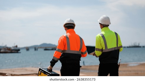 Two industrial workers wearing high-visibility safety jackets and white hard hats carry tool box maintenance operation at a industrial