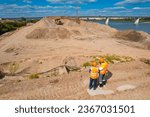 Two industry workers work on sand quarry. Woman use tablet for control excavator, man use radio set.