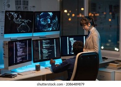Two intercultural programmers consulting about working points while decoding data on computer screen in office