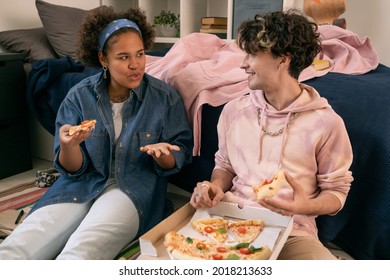 Two Intercultural Teens Discussing Something While Eating Pizza In Home Environment