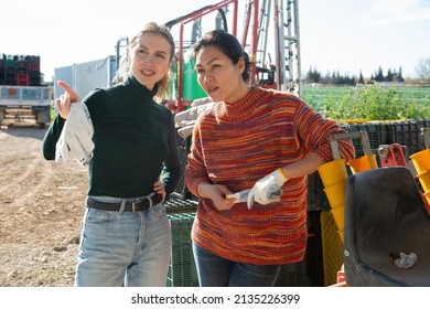 Two Interested Female Farmers Talking While Standing Outdoors Near Farm Machine On Spring Day..