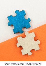 Two interlocking puzzle pieces, one blue and one natural wood, sit on a diagonal white and orange surface. The image evokes connection, teamwork, problem solving and creative collaboration