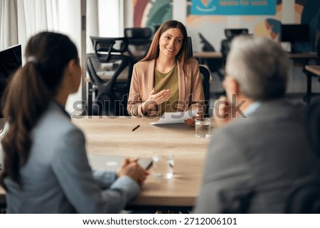 Two interviewers with notebooks converse with a candidate holding her resume, in a professional environment.
