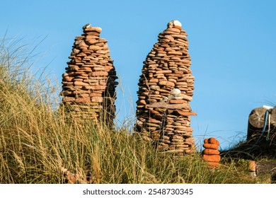 Two intricately stacked stone towers rise from a grassy hill against a clear blue sky, showcasing nature-inspired artistry. - Powered by Shutterstock