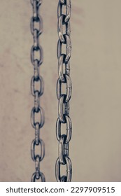 Two iron chains hang vertically on a light background. Iron traction structure. Steel chain. One by one. Male background. Parallel lines.