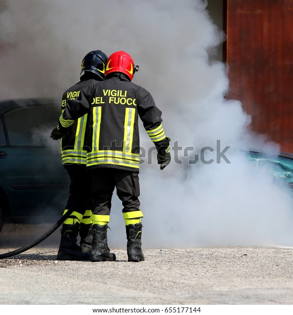 Two Italian fire brigade with the letter on the\
uniform meaning firemen turn off the fire of the car during an\
anti-fire exercise