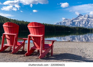 Two Jack Lake With The Iconic Red Adirondack Chairs At The Shoreline In Banff National Park