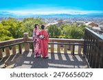 Two Japanese women in kimono overlooking Kyoto from the top of S Azerbai Castle, view over city and mountains, blue sky