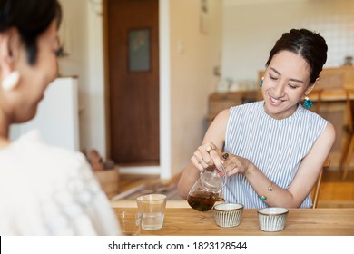 Two Japanese Women Sitting At A Table In A Vegetarian Cafe, Pouring Tea.