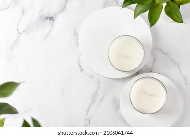 Two Jars Candles With Cococut Or Soy Wax On Table With Vase Of Green Leaves. White Interior Pfotography. Top View, Marble Background