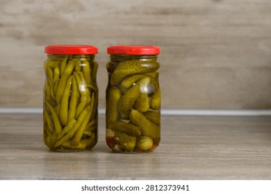 Two jars filled with vibrant pickled green beans and crunchy cucumbers are placed on a rustic wooden table. The rich colors and crisp textures promise a delightful culinary experience perfect for adding zest to any meal.