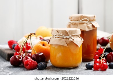 Two jars with peach jam and fresh fruits on stone background. 
