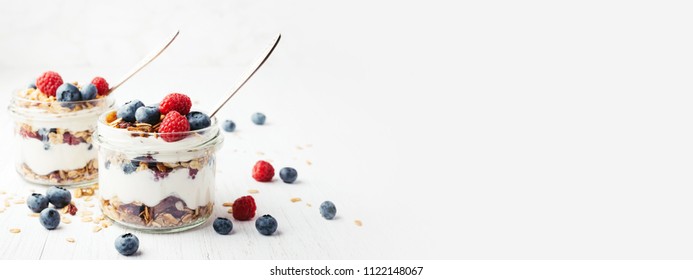 Two jars with tasty parfaits made of granola, berries and yogurt on white wooden table. Shot at angle with place for text, banner. - Powered by Shutterstock