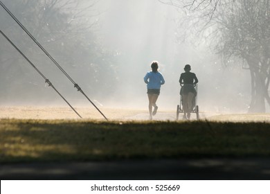Two joggers one with a baby stroller exercise despite the misty fog.