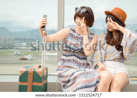 Two joyful cheerful girls taking a selfie while sitting together and showing peace gesture outdoors.