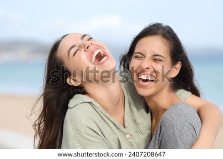 Two joyful friends laughing hilariously on the beacha and hugging