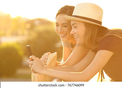 Two Joyful Friends Watching On Line Content In A Smart Phone In A Balcony At Sunset