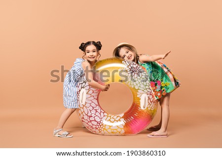 Two joyful little girls in beach outfit with swimming ring in studio