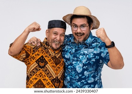 Two joyful men, one in traditional Indonesian batik and kopiah, the other in a Hawaiian shirt, celebrate together. Isolated on white.