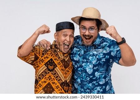 Two joyful men, one in traditional Indonesian batik and kopiah, the other in a Hawaiian shirt, celebrate together. Isolated on white.