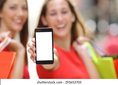 Two Joyful Shoppers With Shopping Bags Showing A Blank Smart Phone Screen In The Street