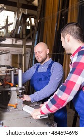Two joyful workers in uniform working on a machine in PVC shop