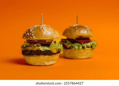 Two juicy mini cheeseburgers with lettuce, onion, tomato, and melted cheese on sesame seed buns, placed against a vibrant orange background. Perfect for fast food, snack, or gourmet concepts. - Powered by Shutterstock