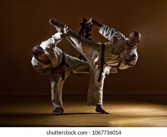 Two Karate Men Fighting In A Indoor Dojo.