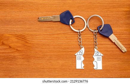 Two Keys With Split House Matching Keychains On A Wooden Table. Splitting Assets In A Divorce.