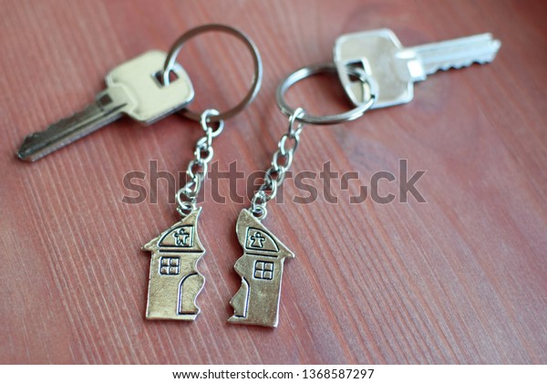 Two keys with splitted broken key rings with\
pendant in shape of house divided in two parts on wooden background\
with copy space. Dividing house at divorce, division of property\
real estate heritage.