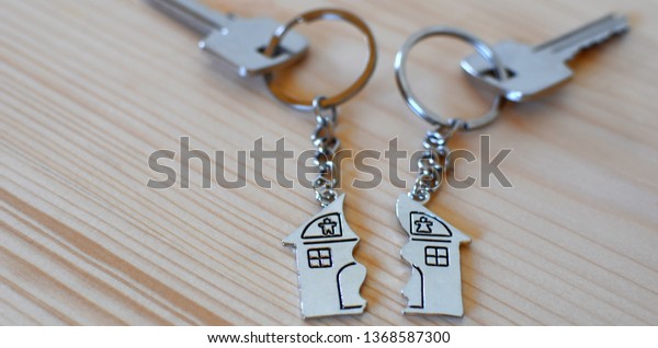 Two keys with splitted broken key rings with
pendant in shape of house divided in two parts on wooden background
with copy space. Dividing house at divorce, division of property
real estate heritage.