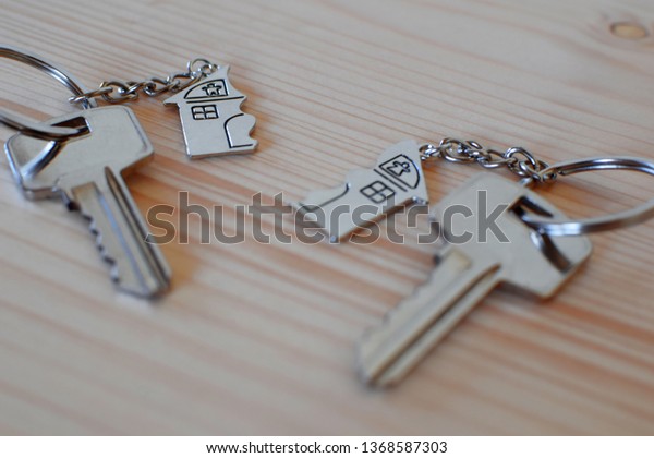 Two keys with splitted broken key rings with\
pendant in shape of house divided in two parts on wooden background\
with copy space. Dividing house at divorce, division of property\
real estate heritage.