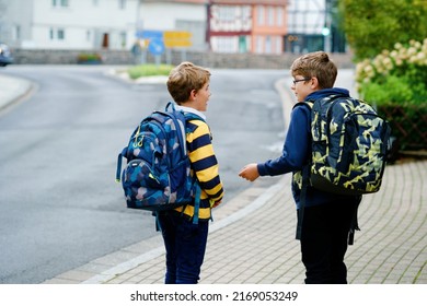 Two kid boys with backpack or satchel. Schoolkids on the way to school. Healthy smiling children, brothers and best friends outdoors on the street leaving home. Back to school. Happy siblings.