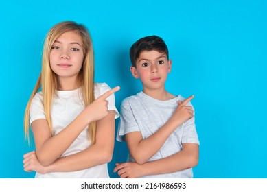 two kids boy and girl standing over blue background smiling broadly at camera, pointing fingers away, showing something interesting and exciting. - Shutterstock ID 2164986593