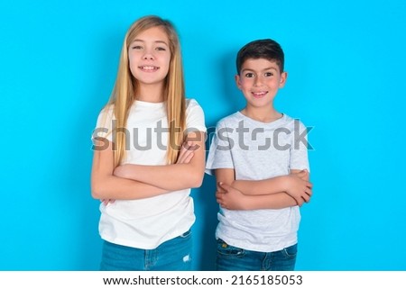 two kids boy and girl standing over blue background being happy smiling and crossed arms looking confident at the camera. Positive and confident person.