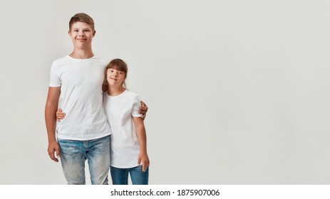 Two kids, disabled boy and girl with Down syndrome smiling at camera, embracing each other while posing together isolated over white background. Children with disabilities and special need concept