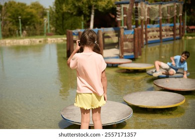 Two kids enjoy an adventurous stepping stone activity in a sunny park. The playful interaction captures the essence of outdoor fun and friendship in nature. - Powered by Shutterstock