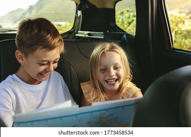 Two kids exploring a map while travel by car. Children going on vacations with their parents.