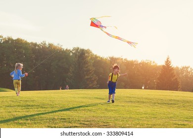 Two Kids Flies A Kite Over Sunset In Park