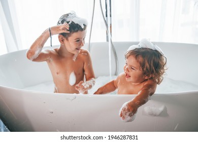 Two kids having fun and washing themselves in the bath at home.