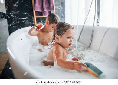 Two kids having fun and washing themselves in the bath at home. Helping each other.