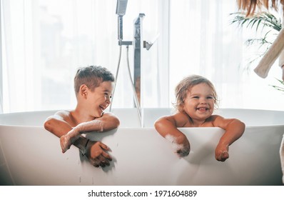 Two Kids Having Fun And Washing Themselves In The Bath At Home. Posing For A Camera.