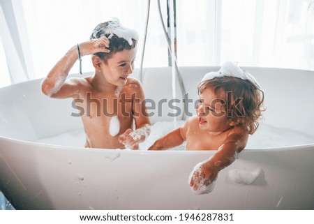 Two kids having fun and washing themselves in the bath at home.
