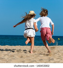 Two kids holding hands running towards sea.