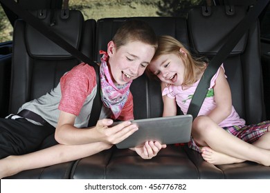 Two Kids On Technology In The Back Of A Car