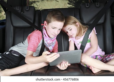 Two Kids On Technology In The Back Of A Car