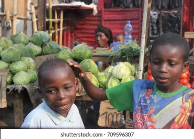 Two Kids Play In The Street Near A Veg And Fruit Market In The Outskirts Of Kinshasa, Democratic Republic Of Congo. July 2015. Poverty Is An Endemic Issue Across The DRC. 