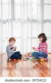 Two Kids Playing With Wooden Blocks In Front Of Window